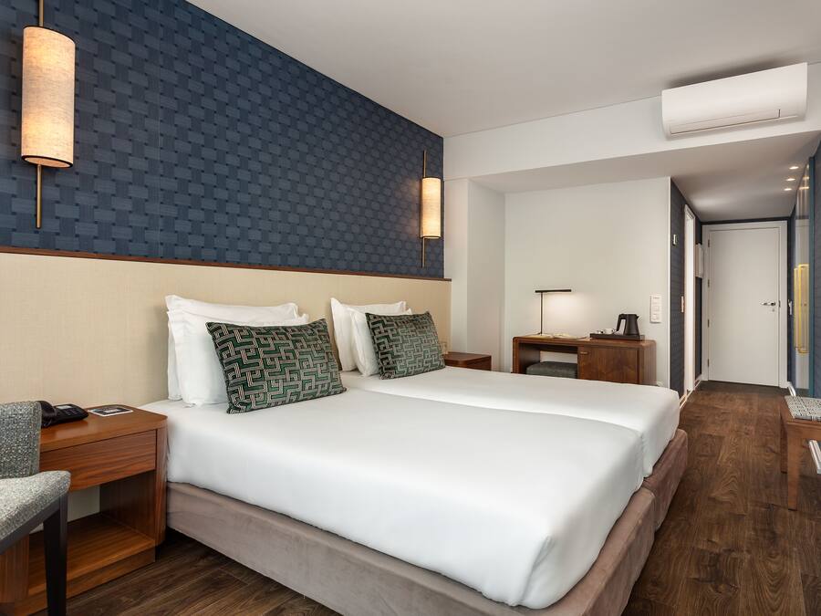 Una habitación de hotel con una cama grande, dos mesitas de noche, un escritorio, una silla y un televisor.