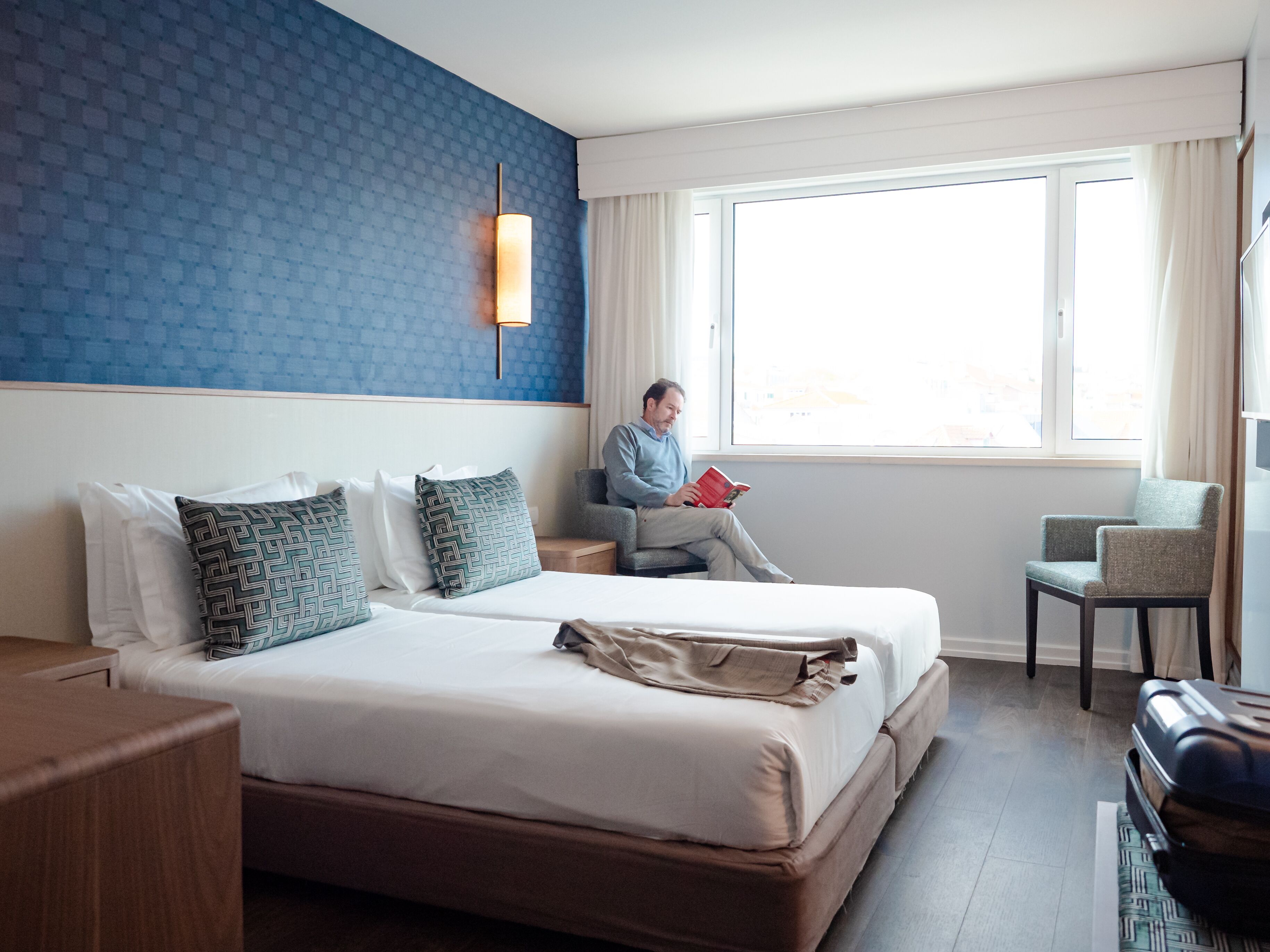 Et hotelværelse med en stor seng, et natbord, en stol og et vindue med gardiner.