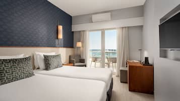 Habitación de hotel con dos camas, un escritorio, una silla y vista al mar.