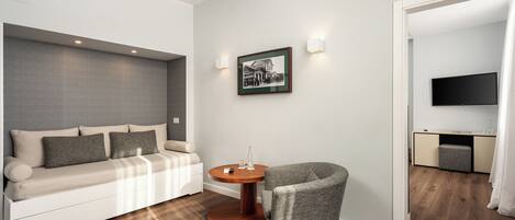 Quarto moderno com sofá, mesa redonda de madeira, cadeira, quadro emoldurado e televisão.