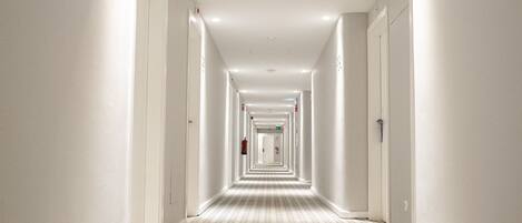 Un long couloir étroit, typique des hôtels, avec un tapis à motifs et des murs blancs.