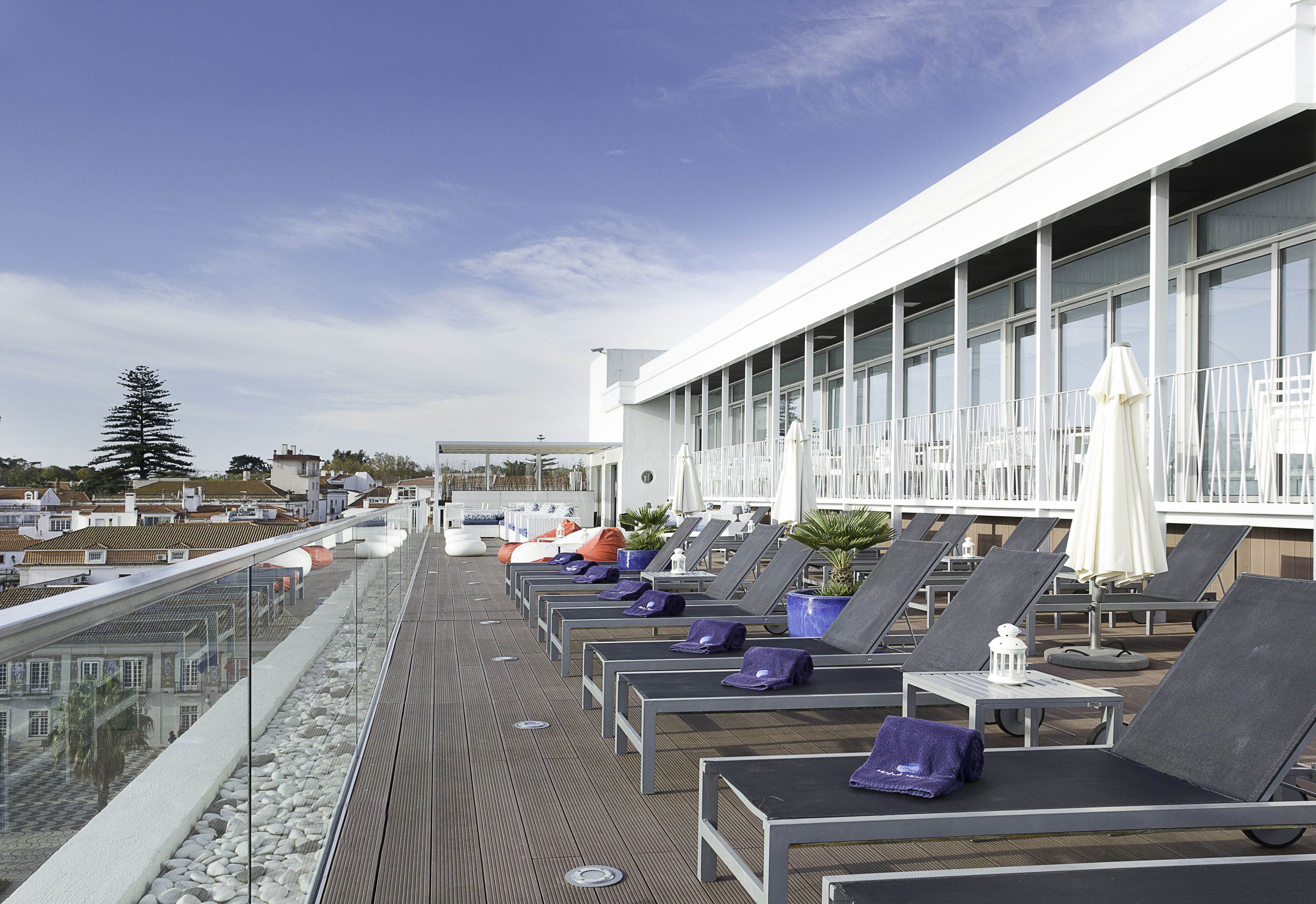 A rooftop terrace with sun loungers, potted plants, and a view of the cityscape.