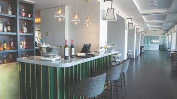 A bar area with a counter, bar stools, hanging pendant lights, and shelves with bottles.