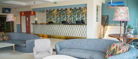 A lobby with a reception desk, sofas, armchairs, a coffee table, and a staircase.