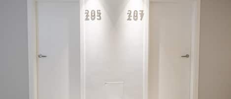 Un pasillo con dos puertas identificadas con los números 205 y 207, un suelo estampado y una lámpara sobre ellas.