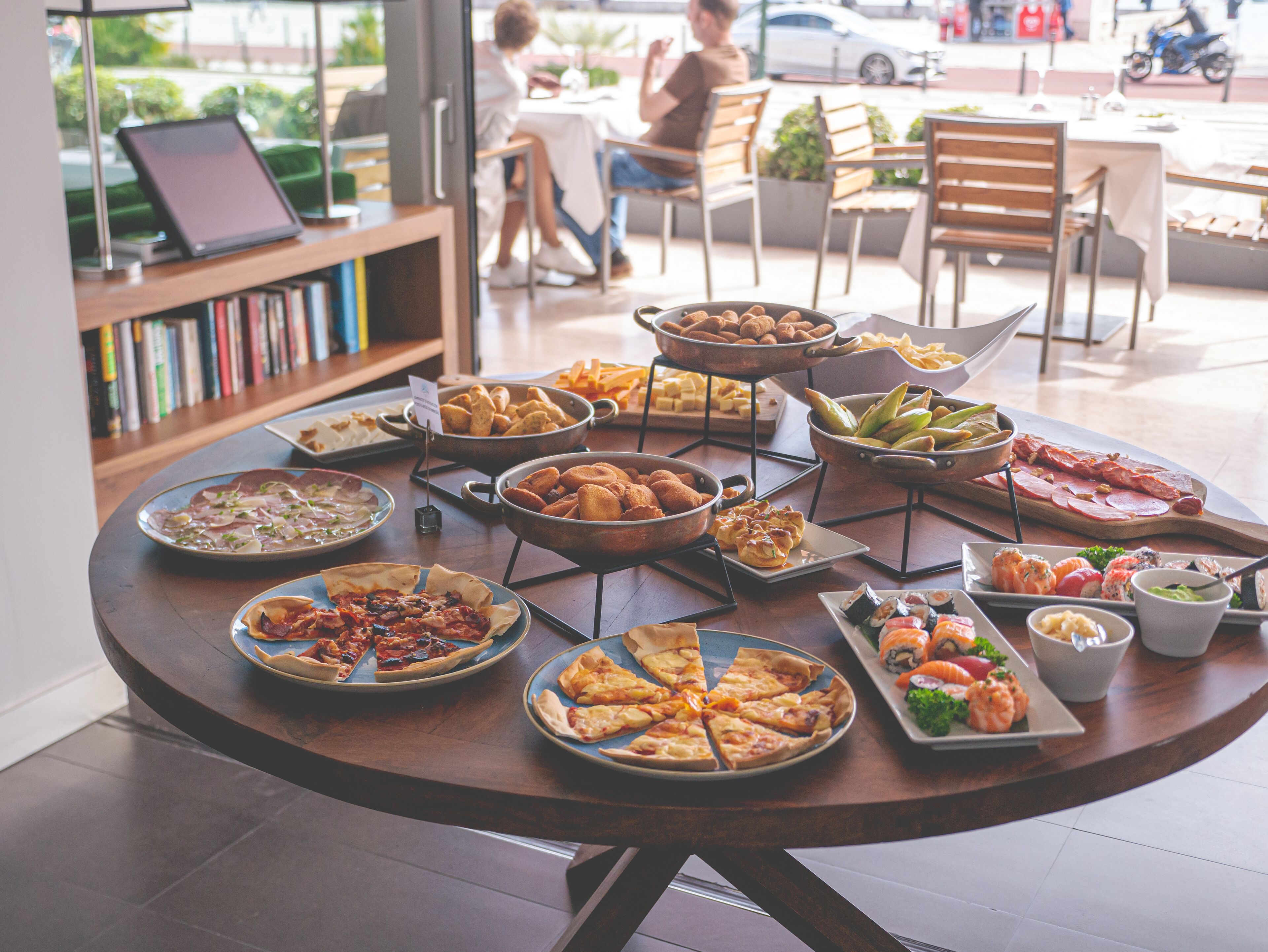Une table ronde sur laquelle sont disposés divers aliments, notamment des pizzas, des sushis et des amuse-gueules.