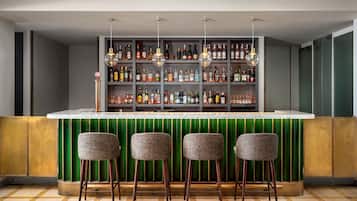 Angolo bar con un bancone verde, numerose bottiglie di liquori e tre sgabelli da bar.