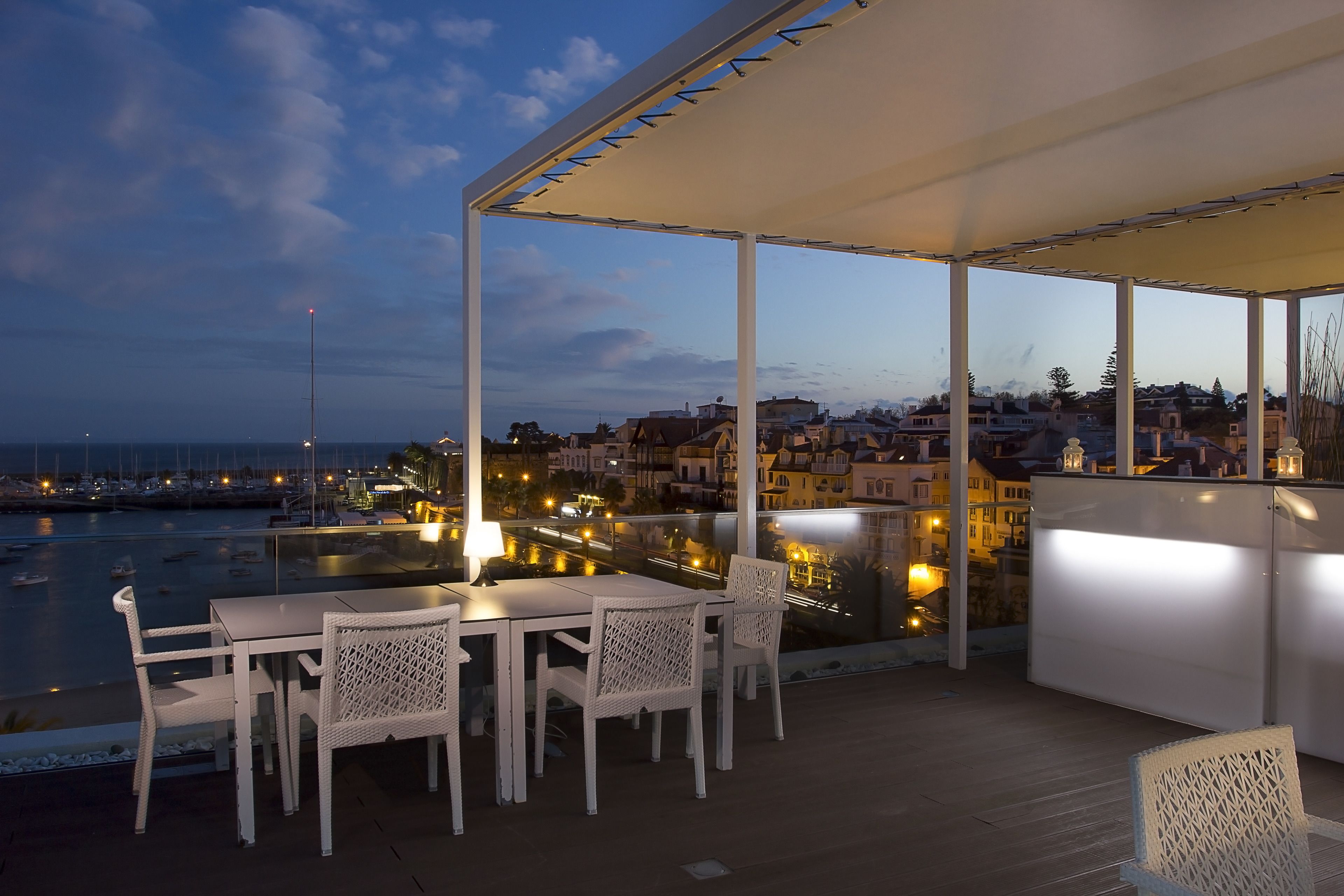Terraço ao ar livre com mesa e cadeiras, com vista para um porto e paisagem urbana.