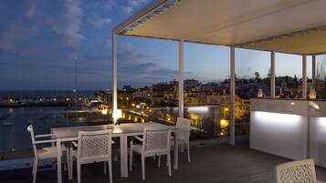 Terraço ao ar livre com mesa e cadeiras, com vista para um porto e paisagem urbana.