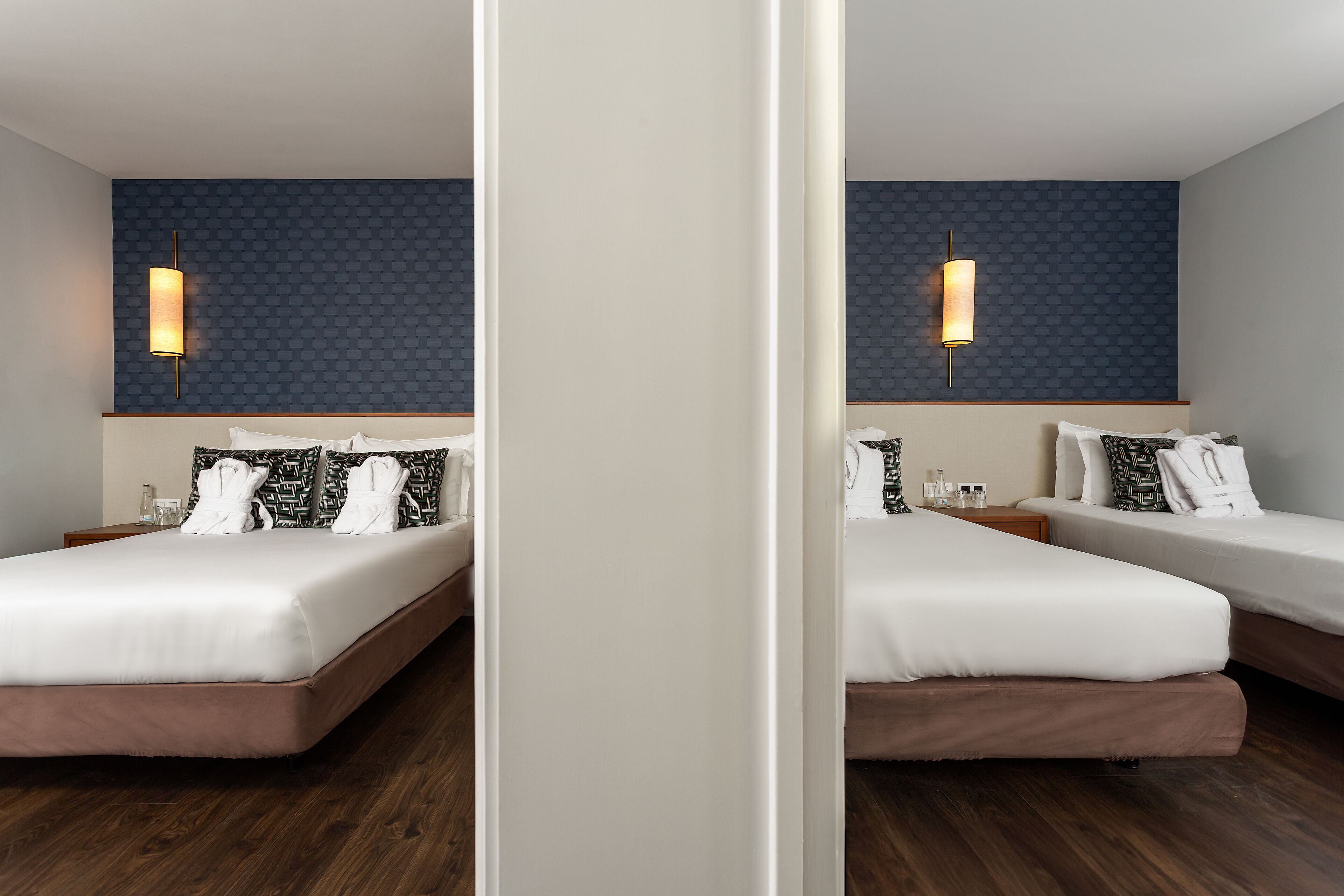 A hotel room with two beds, a dark patterned wall, and a wall-mounted light fixture.