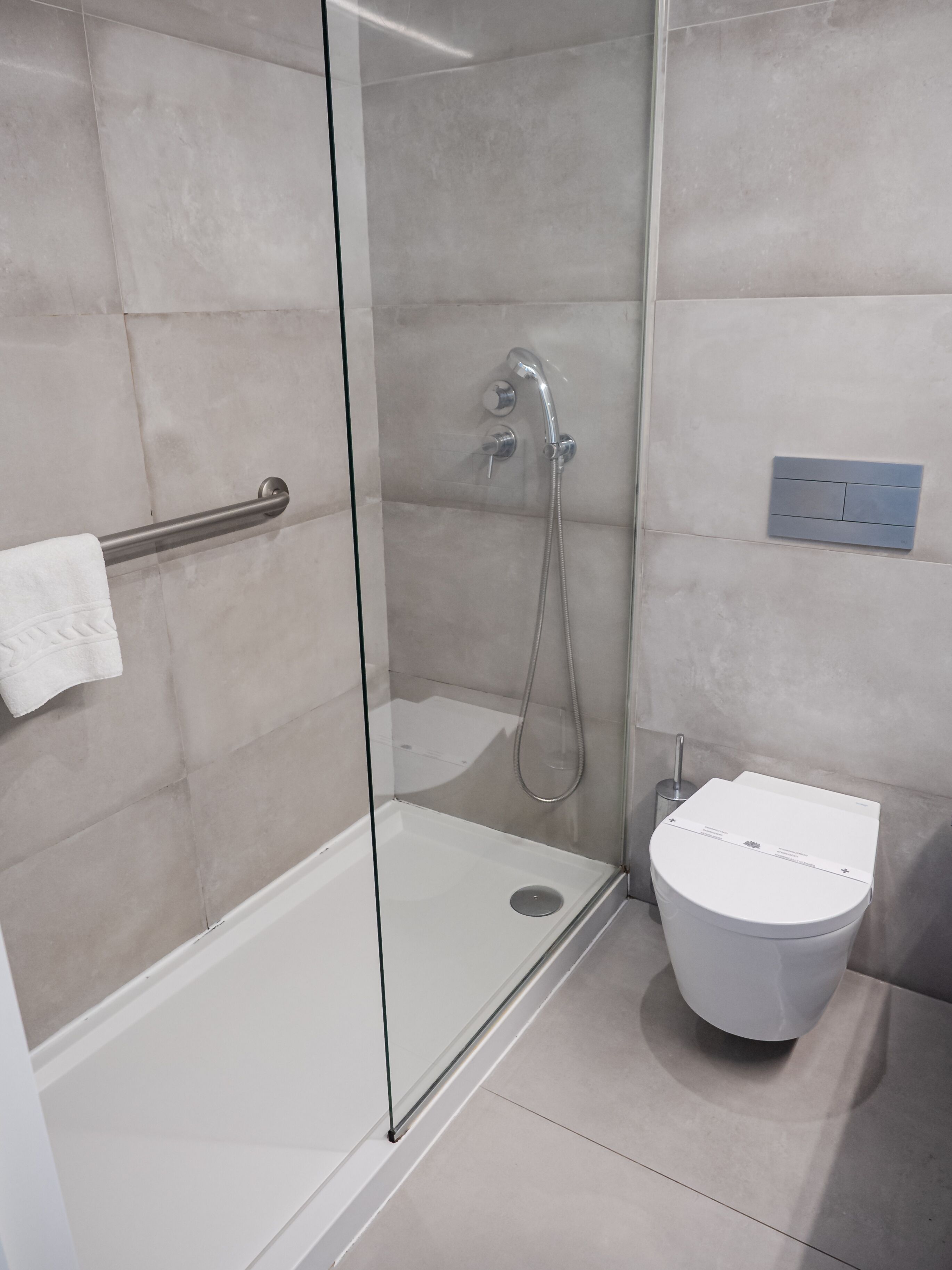 Un baño moderno con cabina de ducha de vidrio, inodoro blanco y un perchero para toallas.