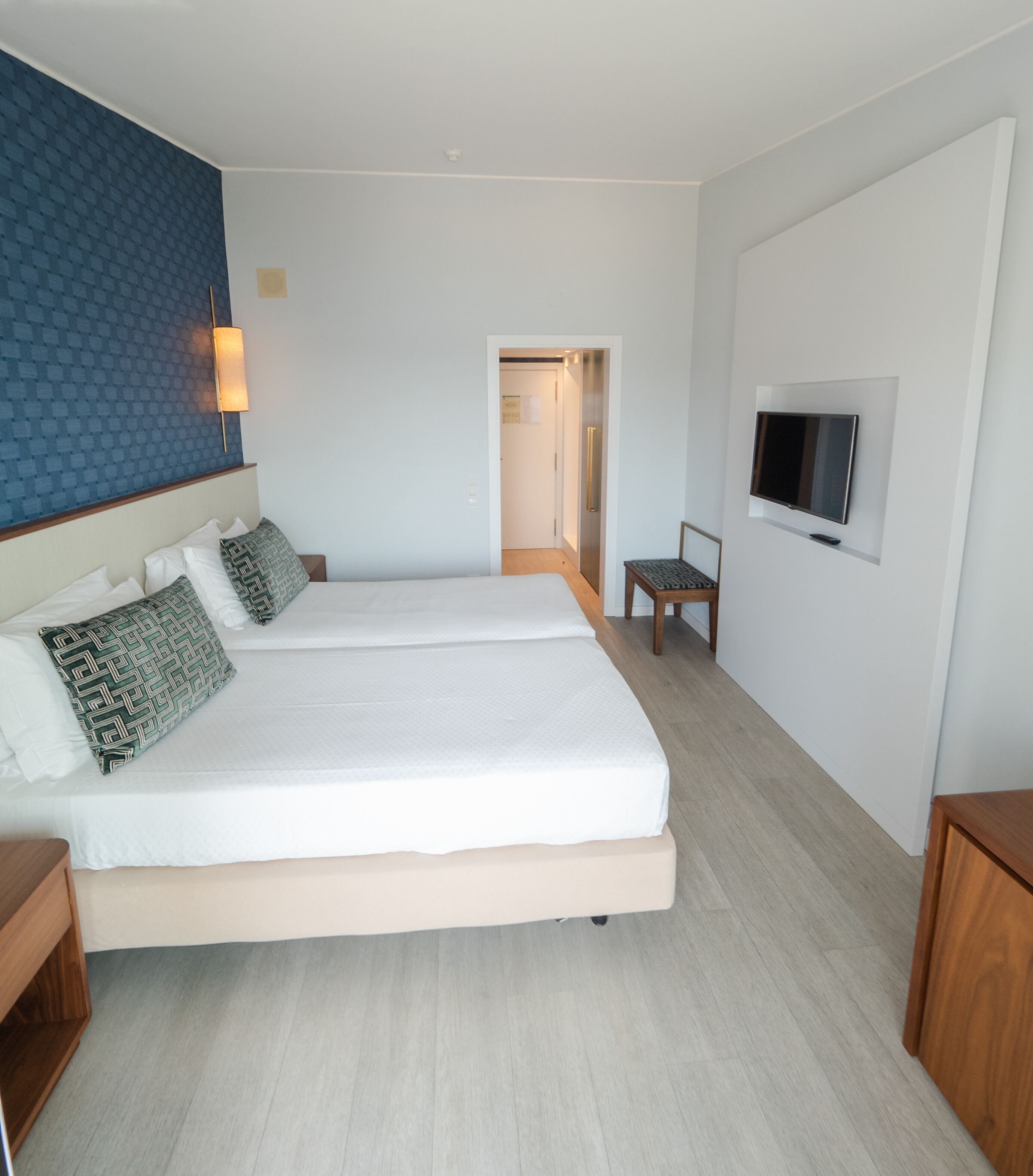 A modern hotel room with two beds, a TV, and a wooden floor.