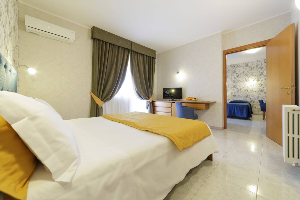 A hotel room with a bed, a desk, a television, and a bathroom visible through an open door.
