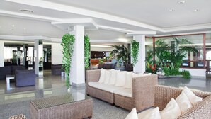 A spacious lobby with a modern design, featuring a large wicker sofa, a glass coffee table, and several potted plants. - Hotel Setar (Quartu Sant'Elena)