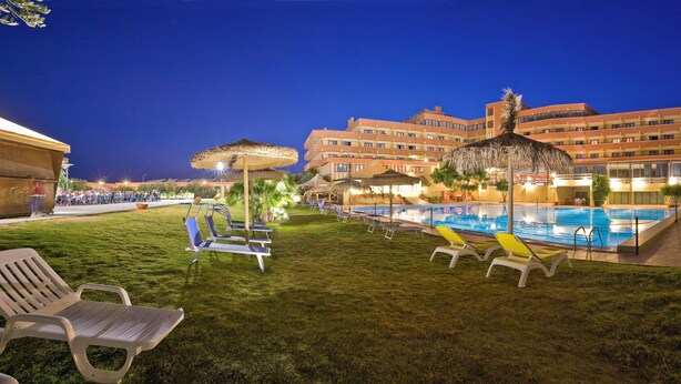A hotel pool area with lounge chairs, a large building in the background, and a well-maintained lawn. - Hotel Setar (Quartu Sant'Elena)