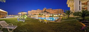 A hotel pool area with lounge chairs, a large building in the background, and a well-maintained lawn. - Hotel Setar (Quartu Sant'Elena)
