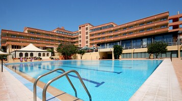 Un hotel con piscina, varios balcones y una zona cubierta con sombrillas.