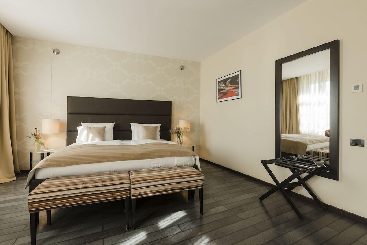 Een hotelkamer met een groot bed, nachtlampjes, een spiegel en een bank.