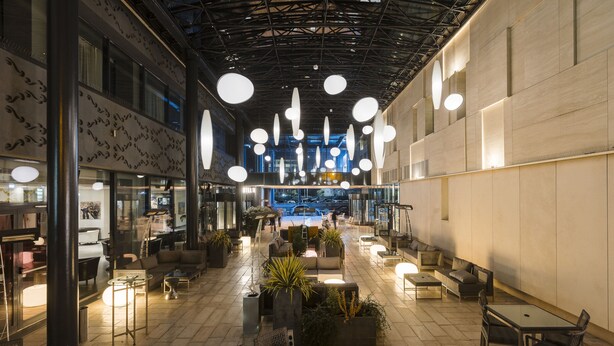 Un espacio interior con techo alto, luces esféricas colgantes y diferentes opciones de mobiliario, incluyendo mesas y sillas.