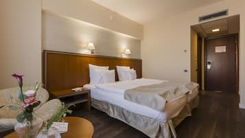 Hotellihuone, jossa on suuri sänky, yöpöytälamput, puinen pääty, yöpöytä, maljakko kukkineen ja kyltti yöpöydällä.
