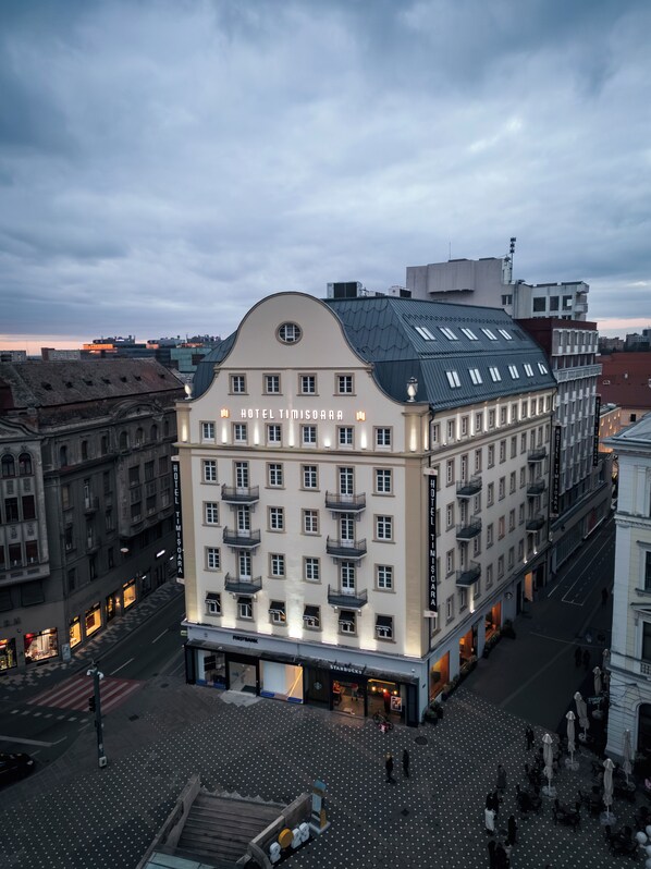 A multi-story hotel with balconies, a central entrance, and a street view.