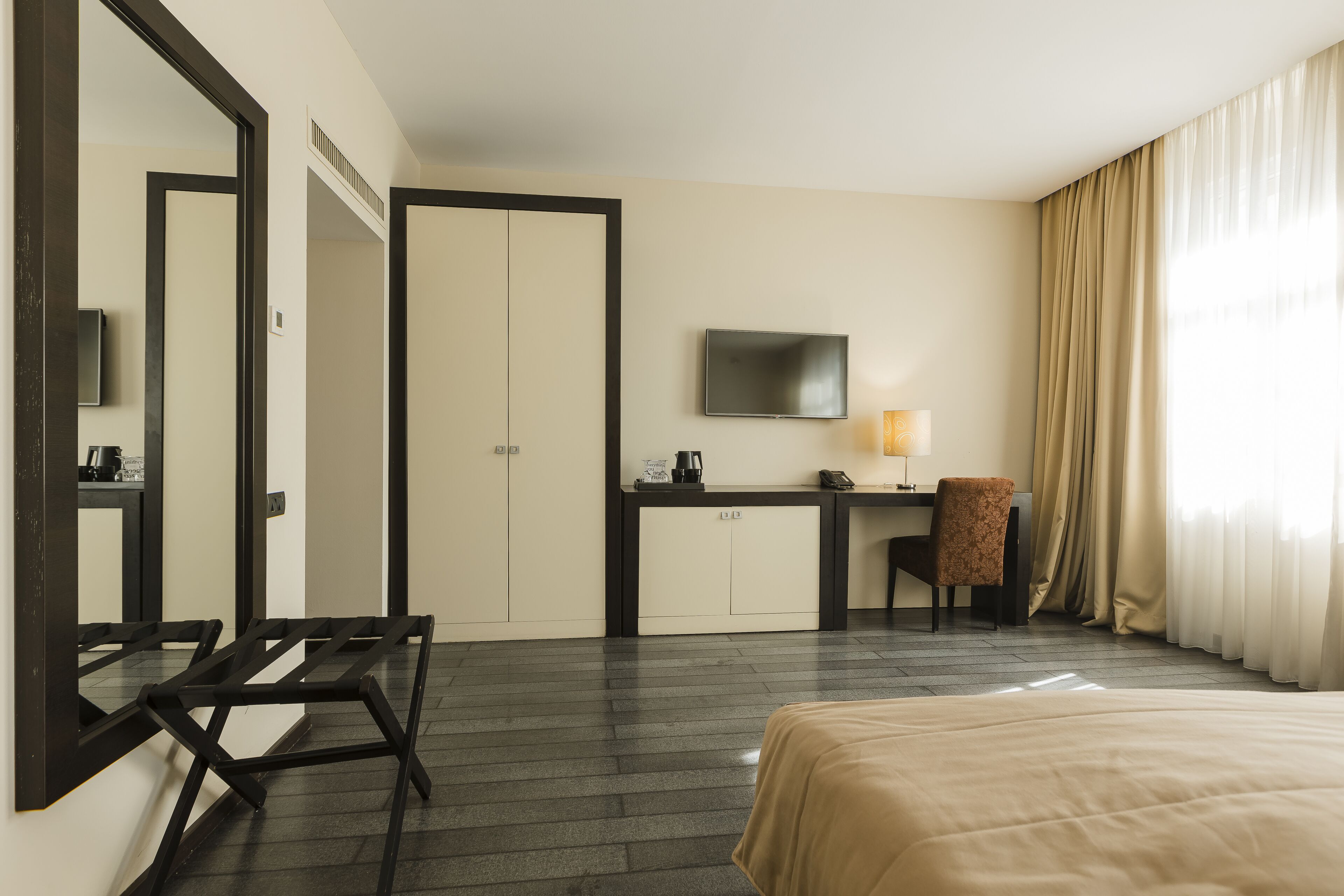 A hotel room with a bed, a desk with a chair, a television, and a large mirror.