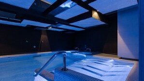Una piscina interior moderna con agua cristalina, una barandilla metálica y suelo de baldosas.