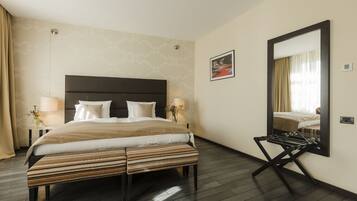 Quarto de hotel com uma cama grande, luminárias laterais, um espelho e um banco.