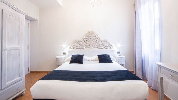 A hotel room with a large bed, a chandelier, a white headboard, and a nightstand with a lamp. - Residenza Florentia (Florence)