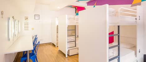 A dormitory room with bunk beds, a desk, and chairs.