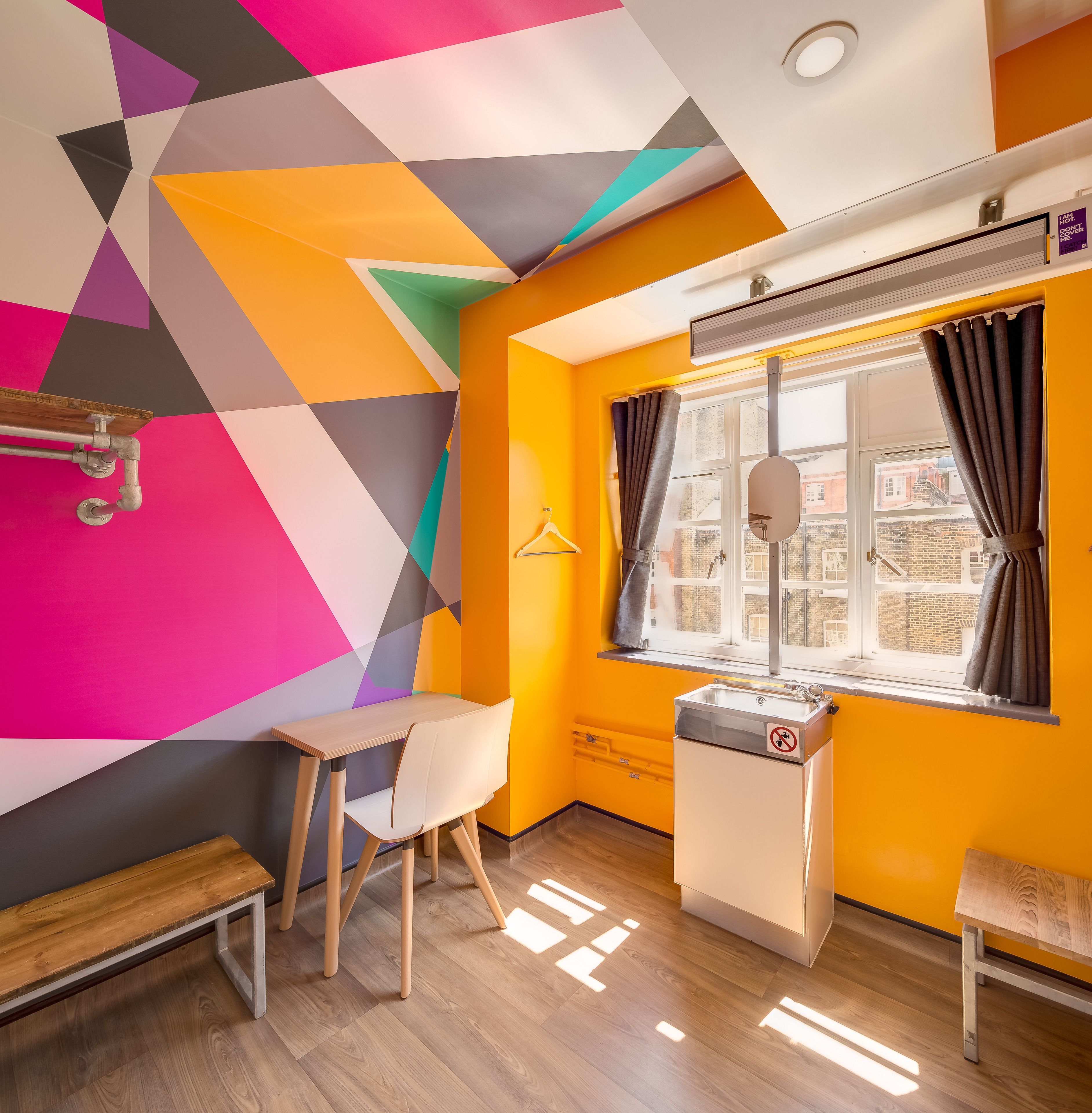 Une pièce avec un motif géométrique sur un mur, une fenêtre avec des rideaux, un lavabo et un banc.