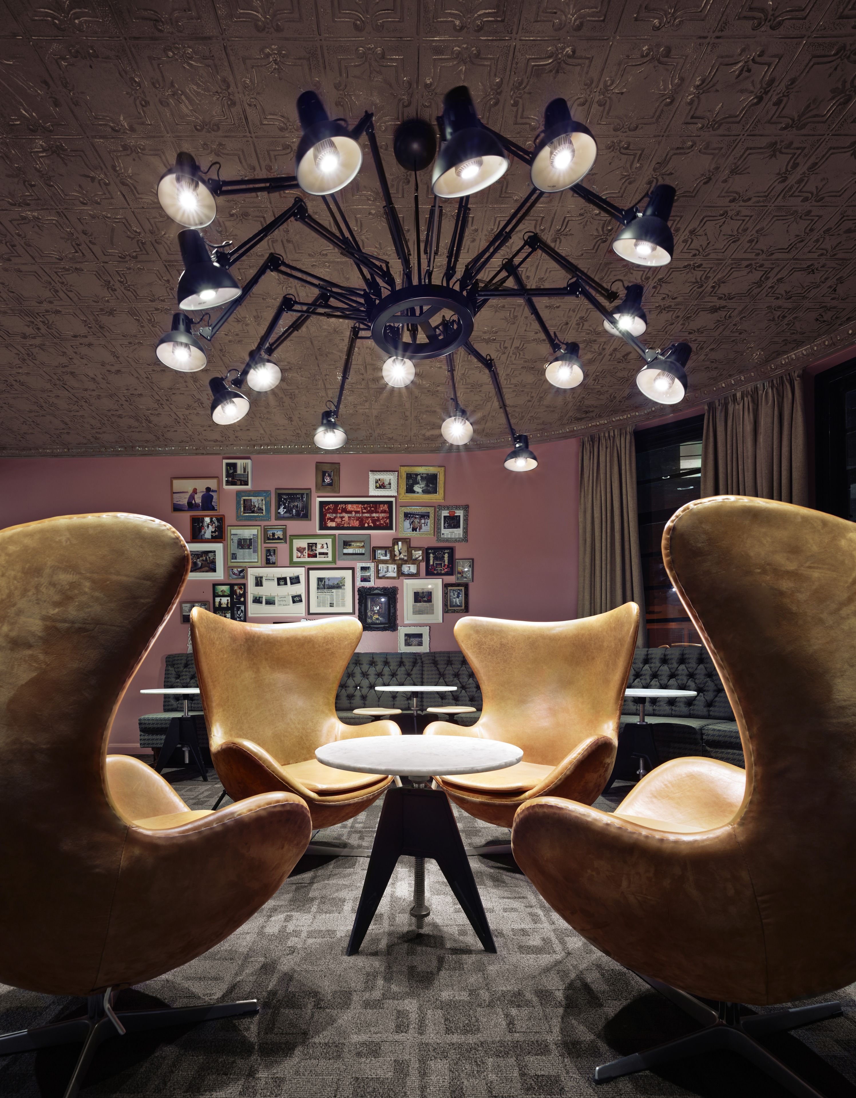 A conference room with a unique ceiling light fixture, a tufted sofa, and a wall adorned with framed photos.