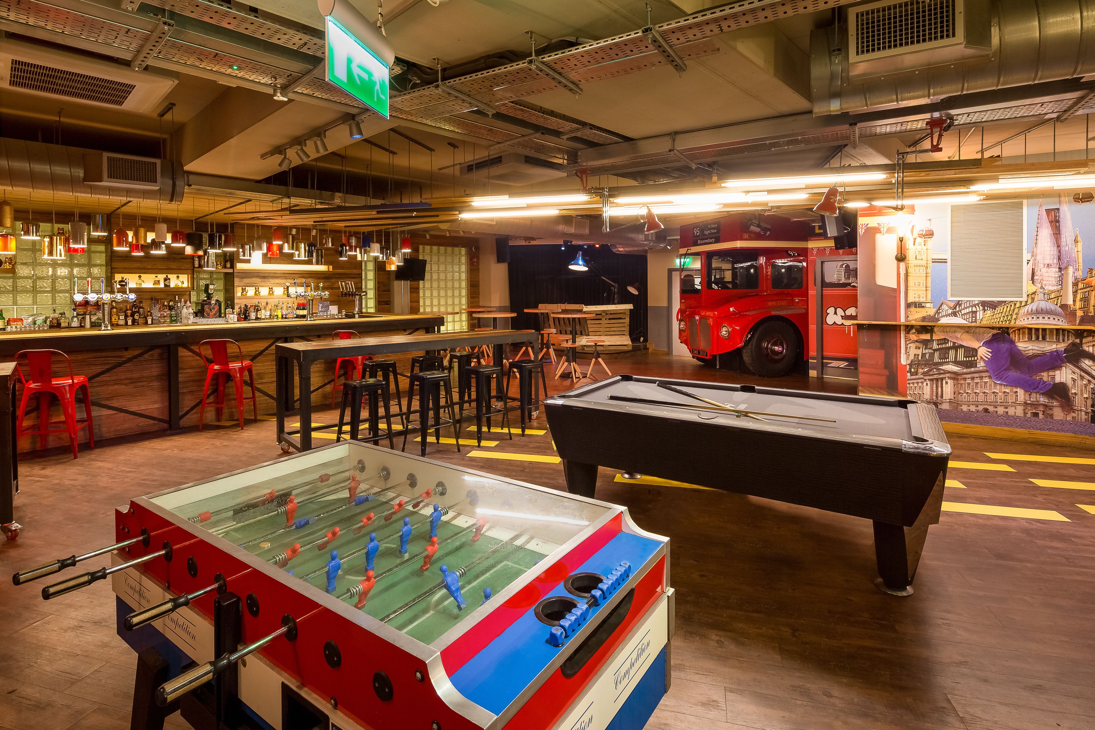 A bar area with a foosball table, pool table, and seating.