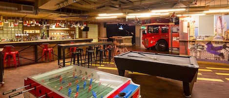 A bar area with a foosball table, pool table, and seating.