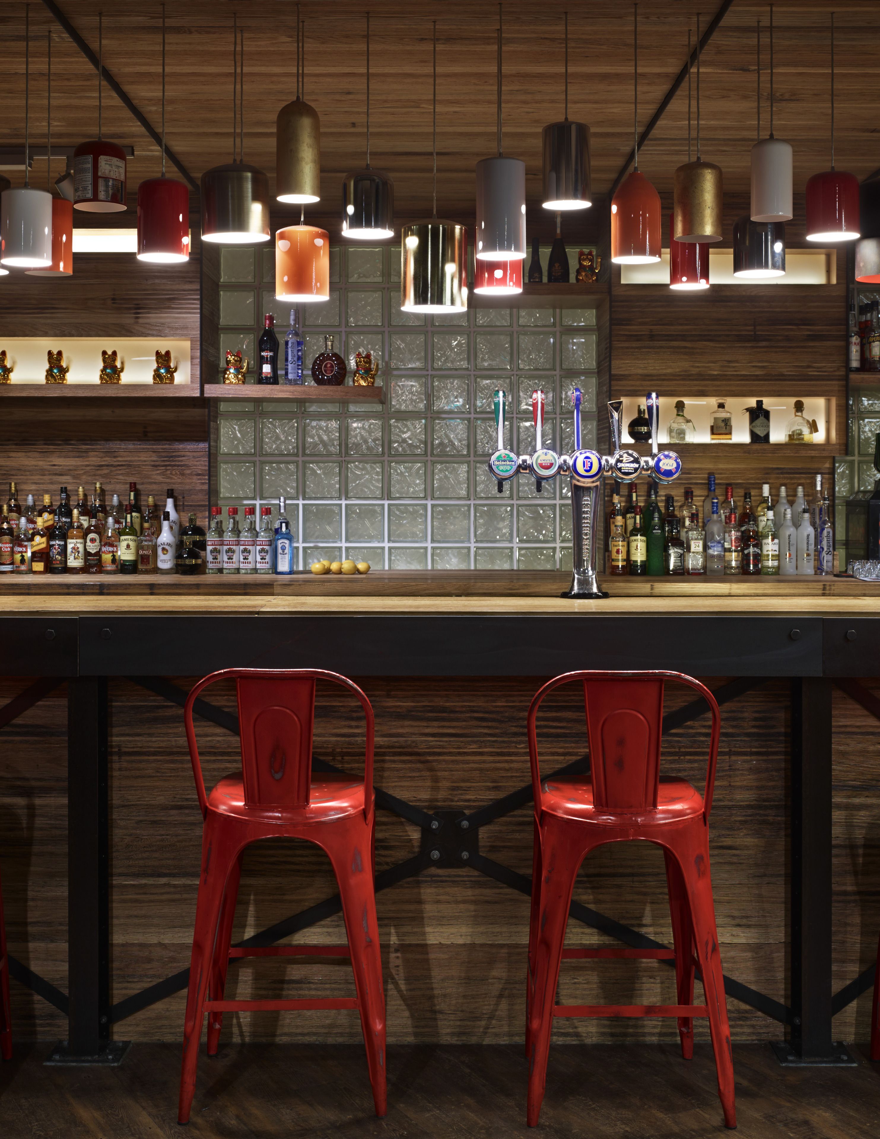 A bar with two red chairs, a wooden counter, and various bottles and beer taps.