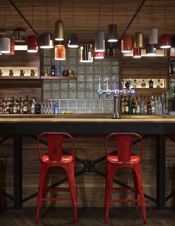 A bar with two red chairs, a wooden counter, and various bottles and beer taps.