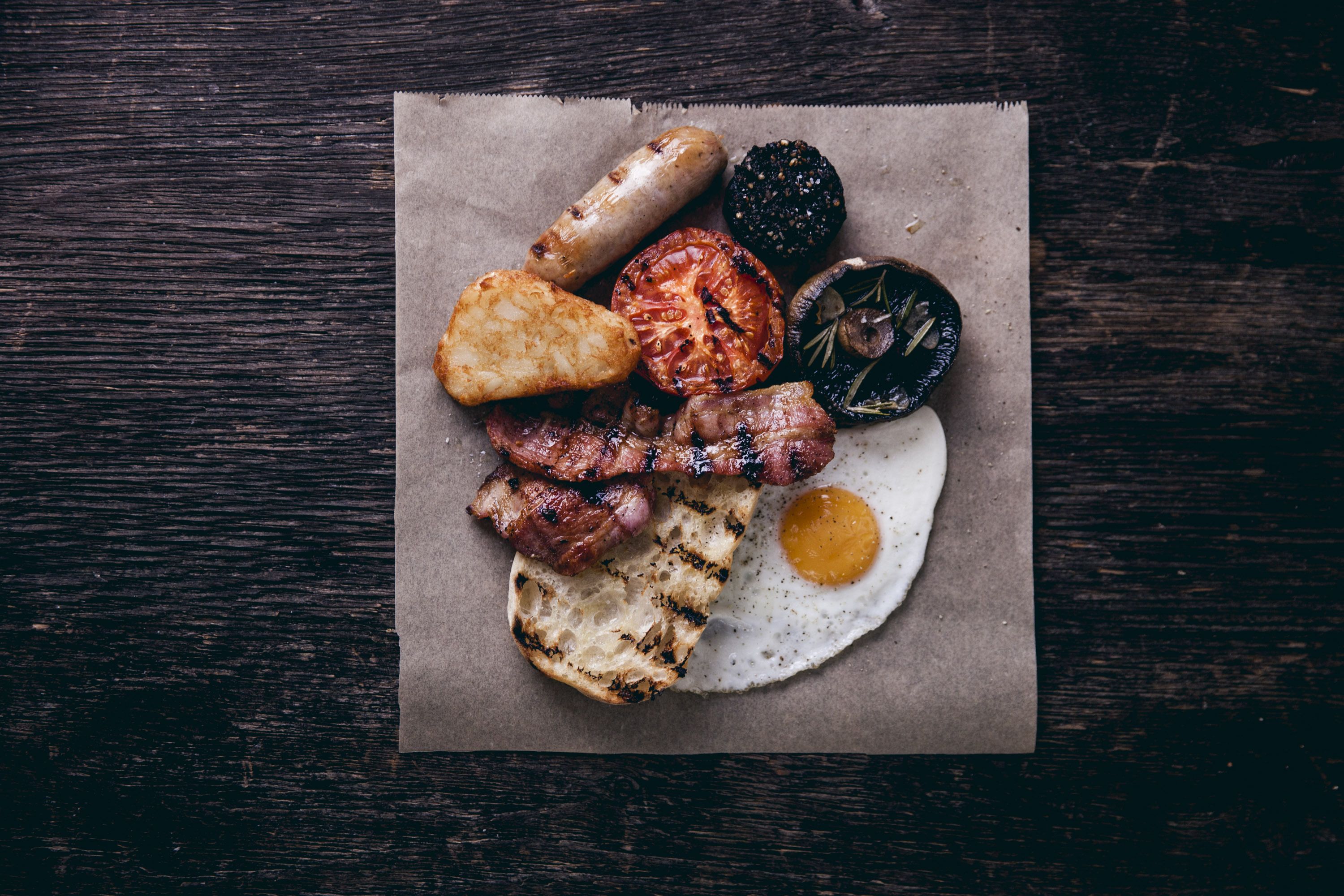 A breakfast plate with various meats, a fried egg, and a slice of toast on a wooden surface.