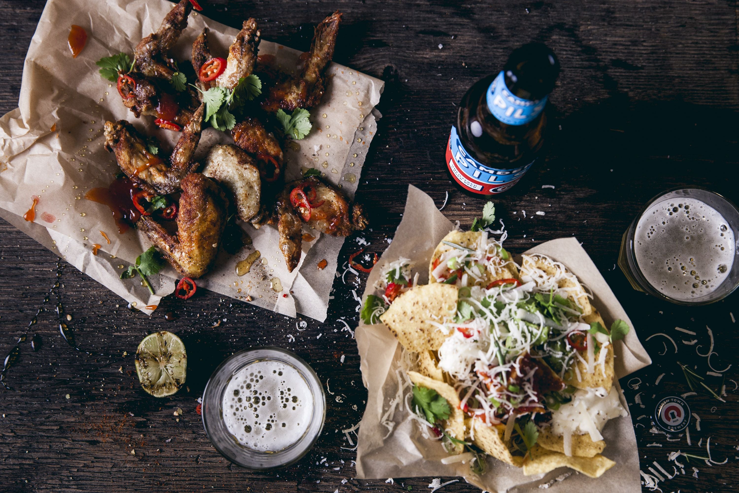A wooden table with food items, a beer bottle, and glasses.