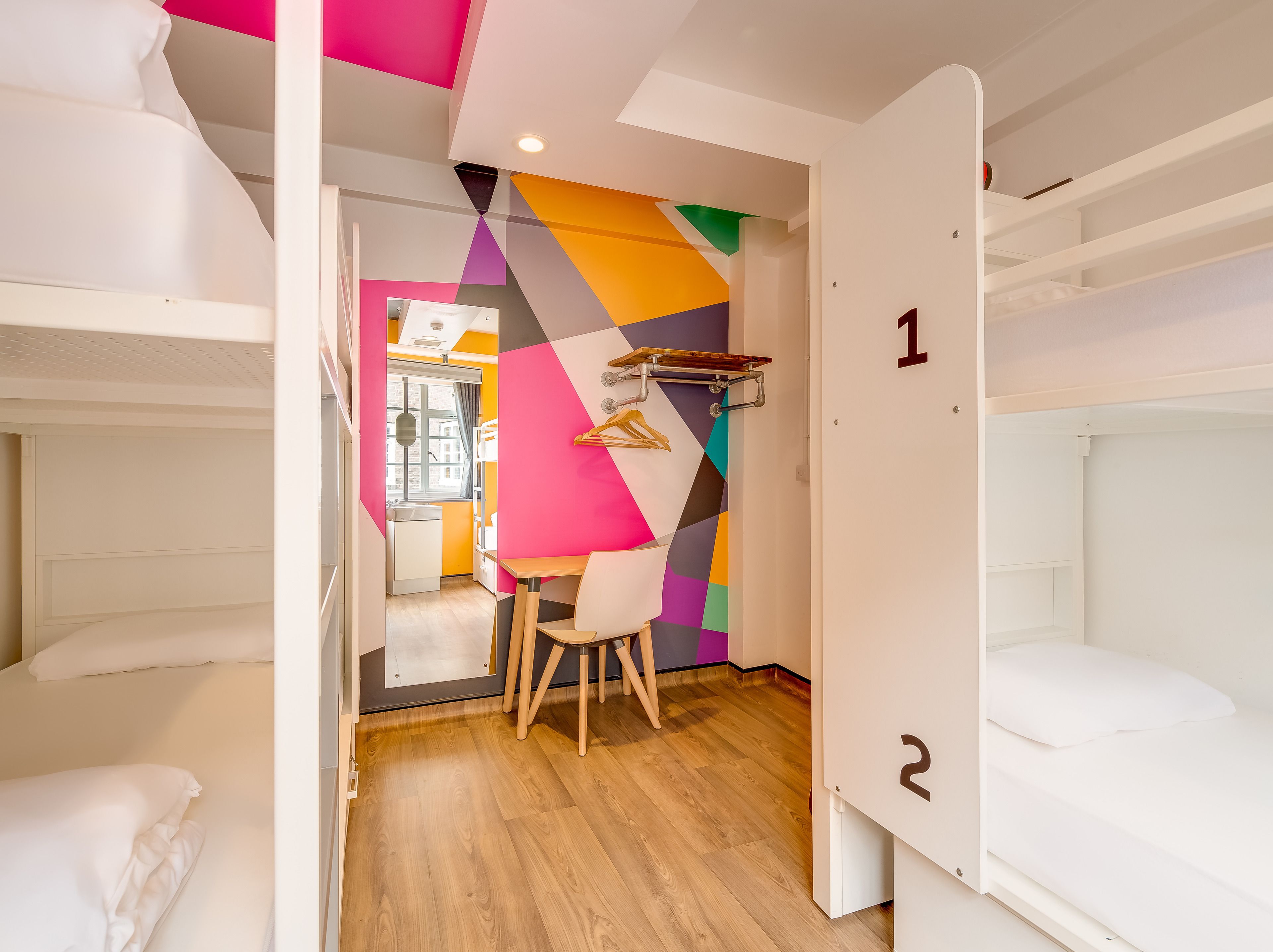 A dormitory room with bunk beds, a desk, and a colorful geometric wall design.