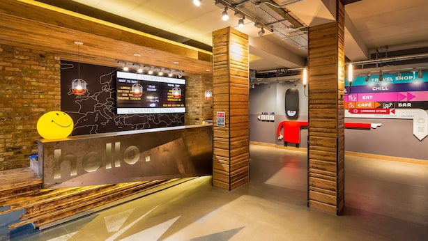 A reception area with a wooden counter, a digital information board, and a luggage store sign. - Generator London (London)