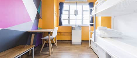 A room with bunk beds, a desk, a chair, and a window with curtains.