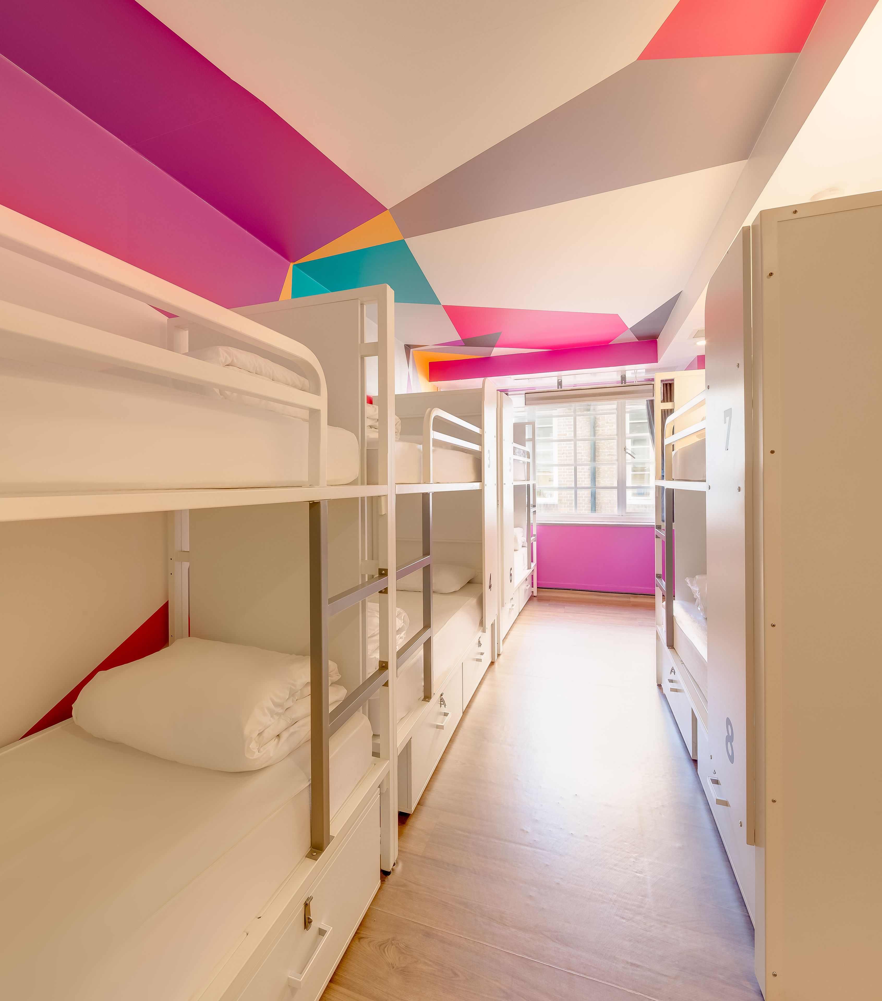 A bunk room with white bunk beds, a wooden floor, and a colorful ceiling design.