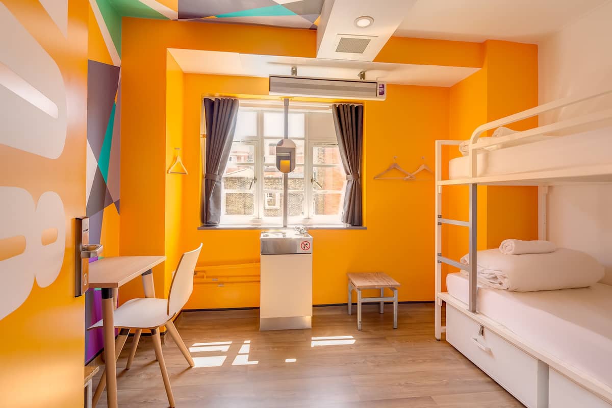 A room with a bunk bed, a desk with a chair, a window with curtains, and a radiator.