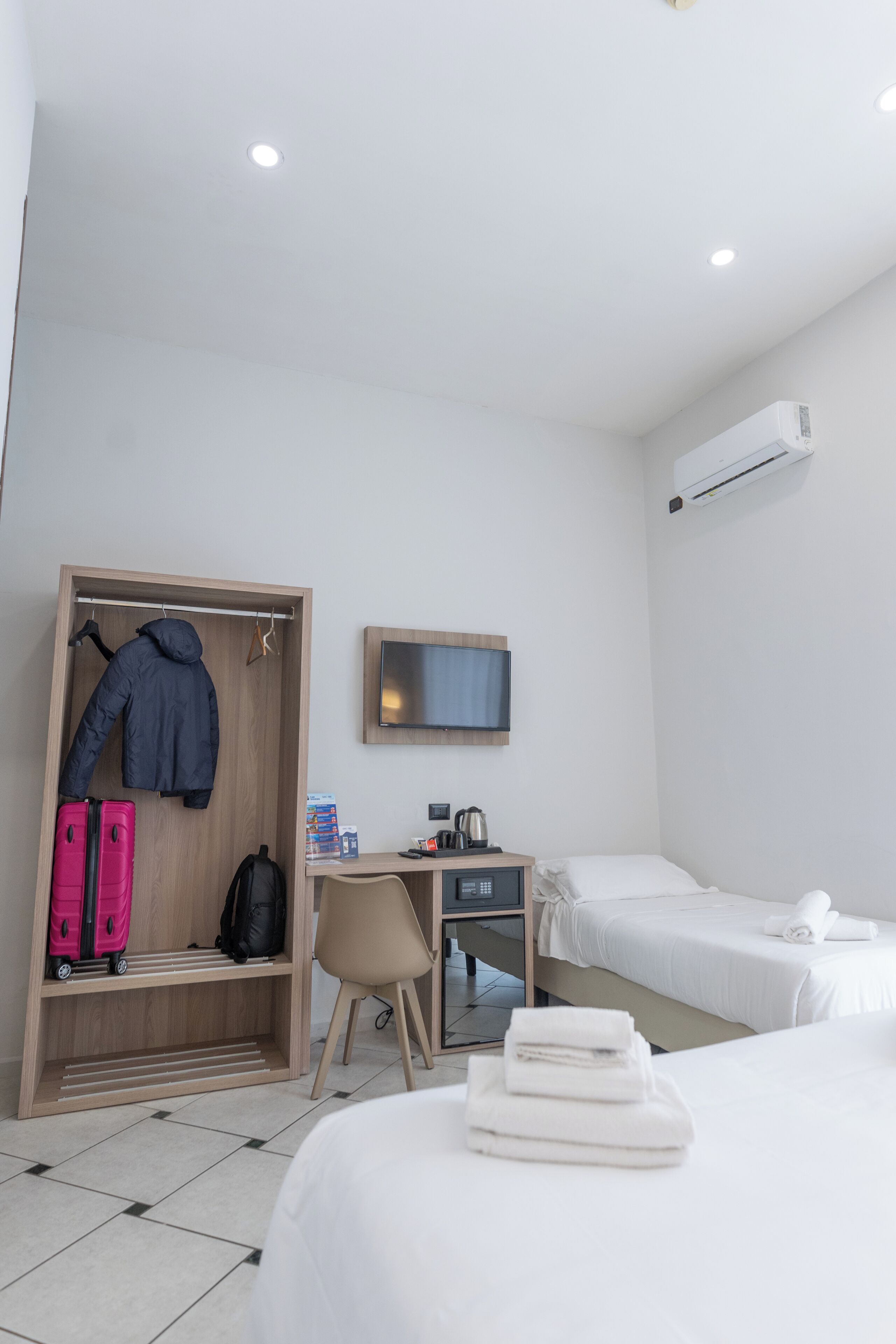 A hotel room with a bed, a desk, a wardrobe, a television, and an air conditioning unit.