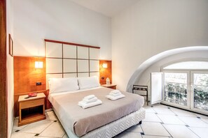 A modern hotel room with a large bed, two bedside tables, a nightstand, and a large window with a view of the city.