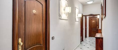Un pasillo con una puerta de madera, un interruptor de luz y una lámpara fijada a la pared.