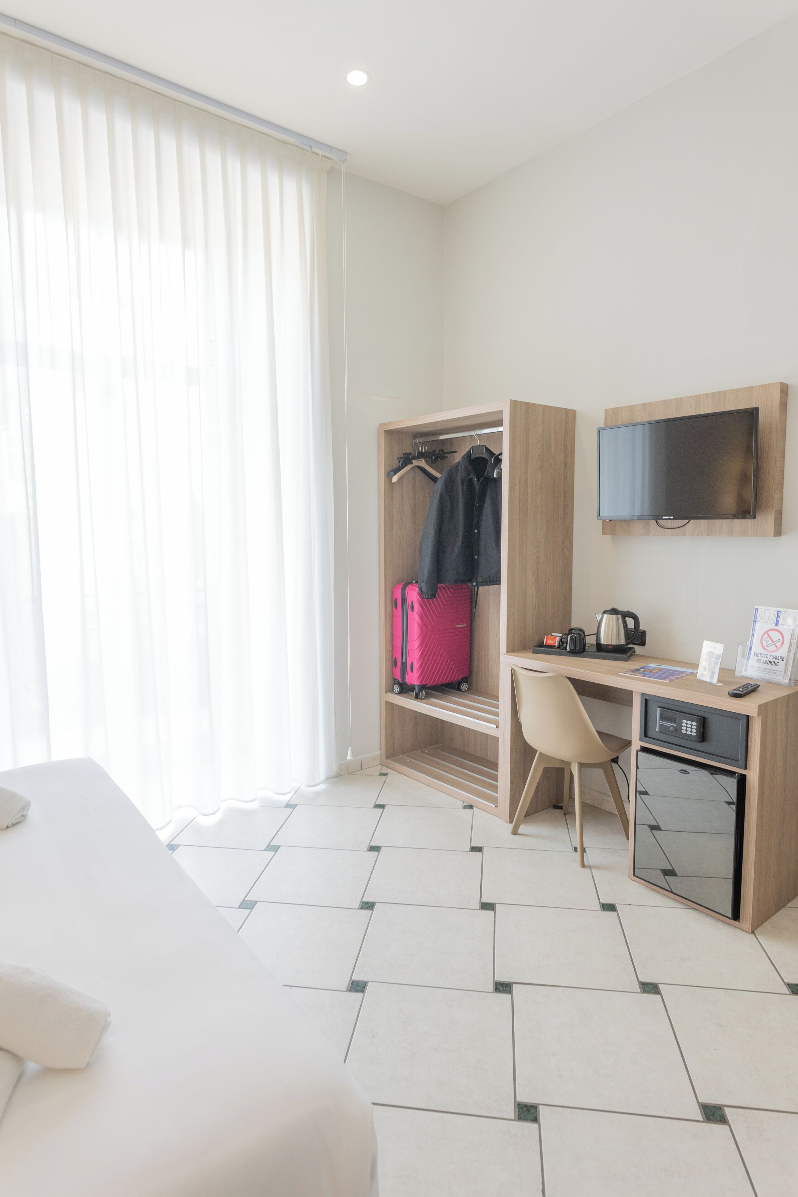 A hotel room with a bed, a desk, a television, a wardrobe, and a suitcase.