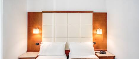 Un lit double avec une tête de lit en bois et deux tables de chevet, chacune équipée d’une lampe et d’un téléphone.