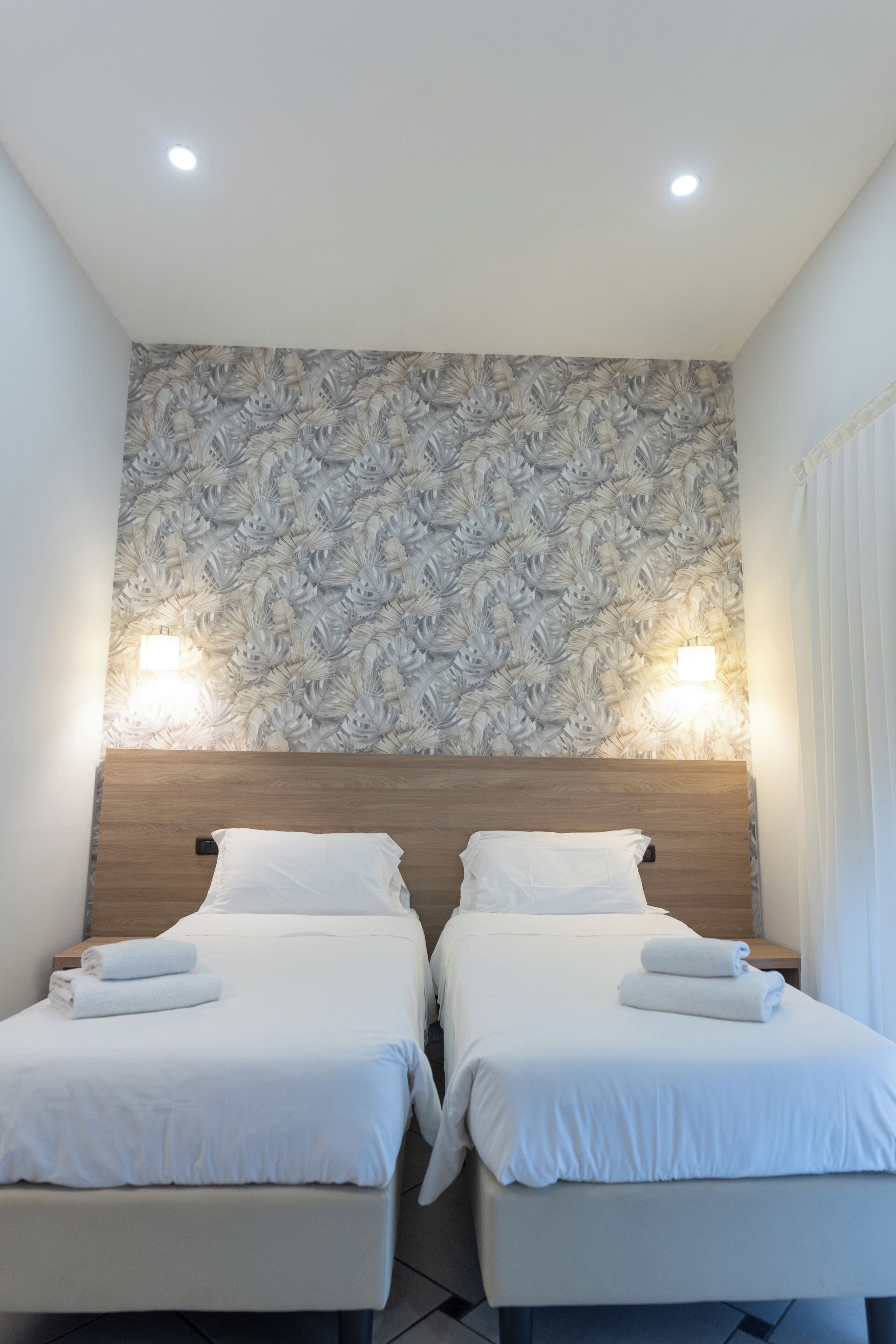 Ein Hotelzimmer mit zwei Betten, einem Holzkopfende und einer Wand mit Blattmuster.