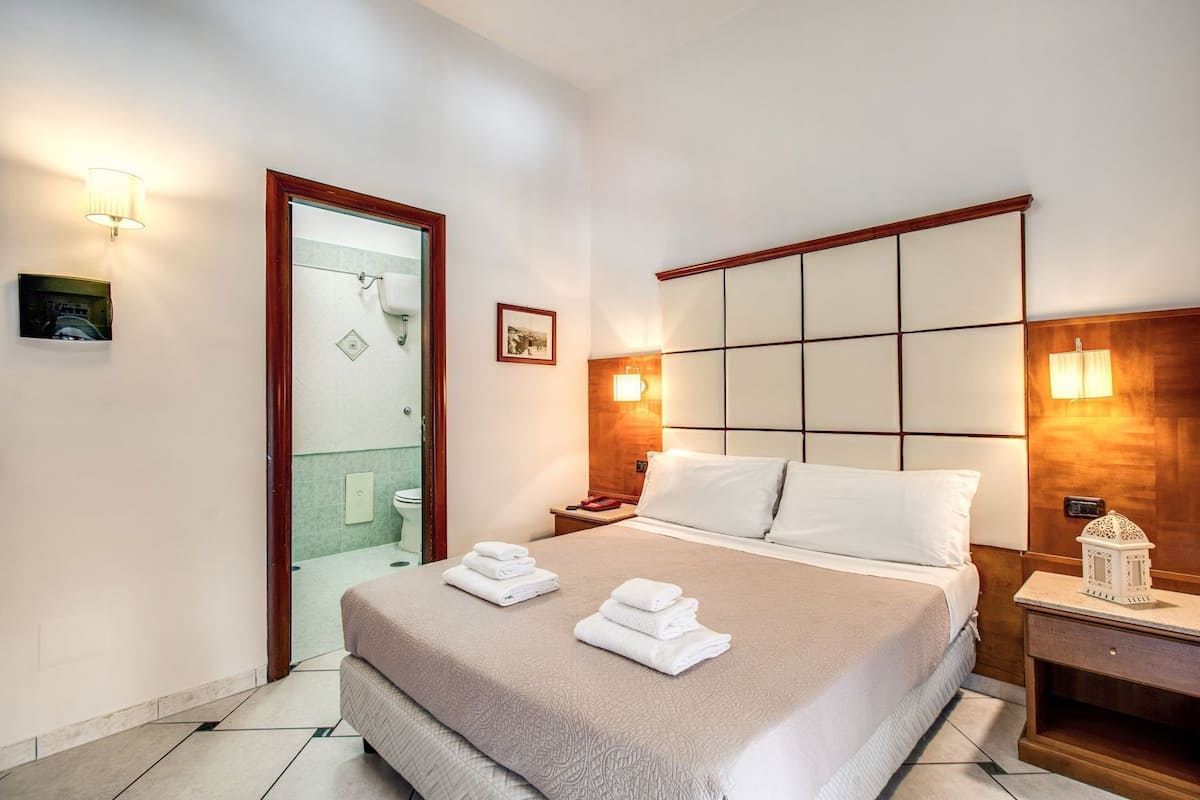 Ein Hotelzimmer mit Bett, Nachttischen, einer Lampe, einem Bild an der Wand und einer Tür zu einem Badezimmer.